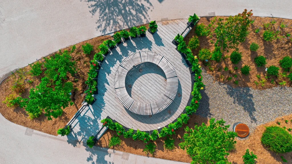 Vue aérienne d'une aire de repos circulaire en bois avec banc intégré, entourée de plantations luxuriantes au Quartier DIX30 à Brossard.